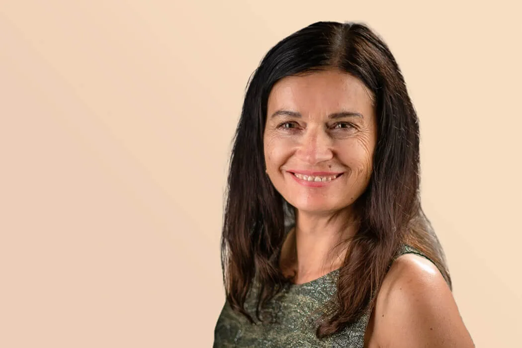 Portrait von Renate Blaschka, lächelnd vor orangenem Hintergrund